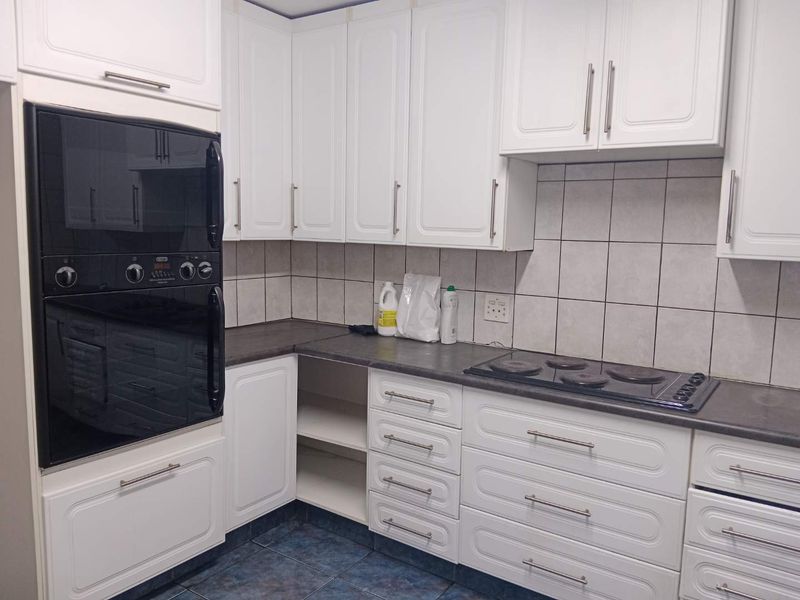 A functional kitchen featuring white cabinetry, dark laminate countertops, a built-in oven, and an electric hob with tiled backsplash and flooring.