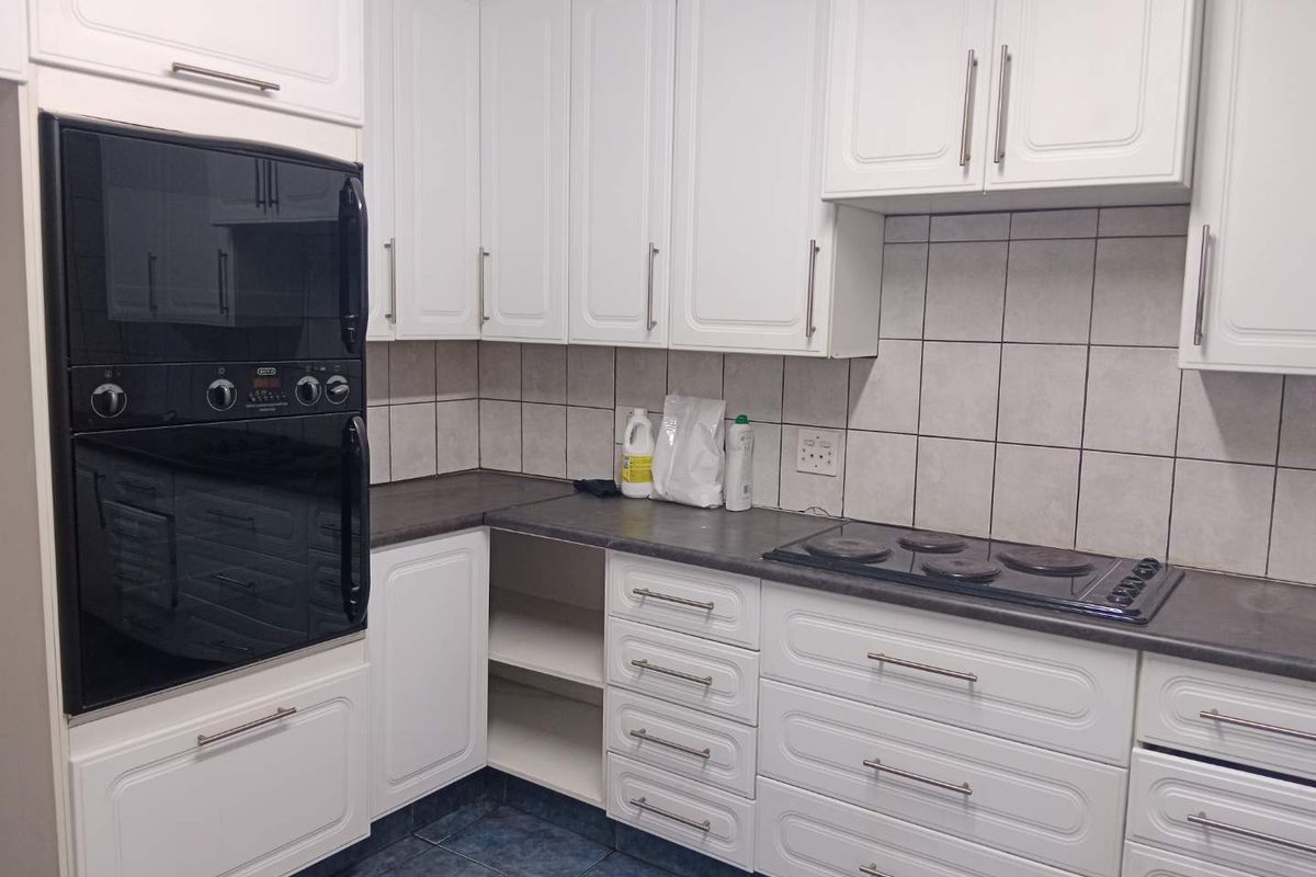 A functional kitchen featuring white cabinetry, dark laminate countertops, a built-in oven, and an electric hob with tiled backsplash and flooring.