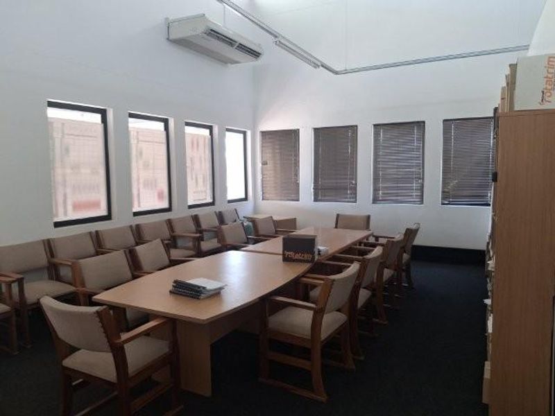 A functional office boardroom featuring a large conference table, multiple chairs, venetian blinds, and a wall-mounted split-system air conditioner.