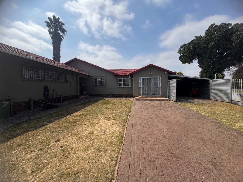 Rear view of the property featuring a paved driveway, attached carport, and a spacious garden area with established trees.