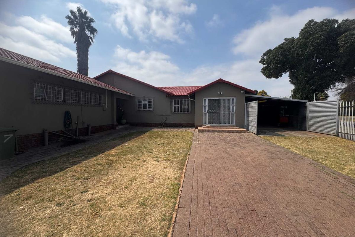 Rear view of the property featuring a paved driveway, attached carport, and a spacious garden area with established trees.