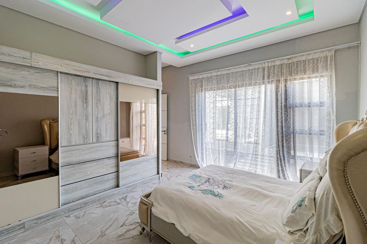 Modern bedroom featuring marble-look tiled flooring, built-in sliding door wardrobes, and a recessed tray ceiling with integrated LED ambient lighting.