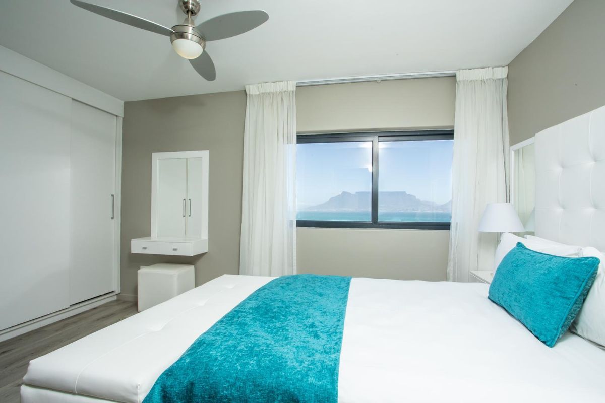 A well-maintained bedroom featuring built-in sliding door wardrobes, a ceiling fan, and a window offering scenic ocean and mountain views.