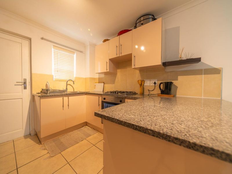A functional kitchen featuring granite countertops, built-in cabinetry, a gas hob, and an integrated oven with tiled flooring and backsplash.