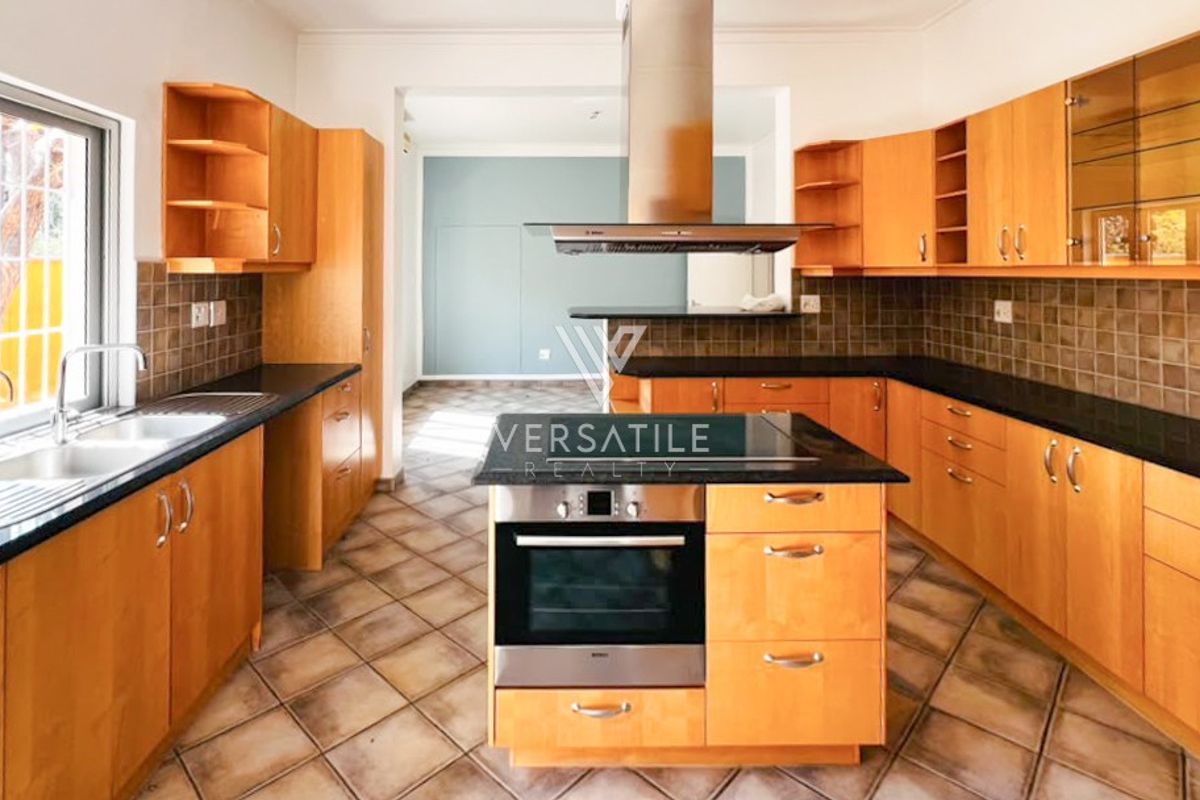 Spacious kitchen featuring wooden cabinetry, granite countertops, a central island with a built-in oven and hob, and a stainless steel extractor fan.