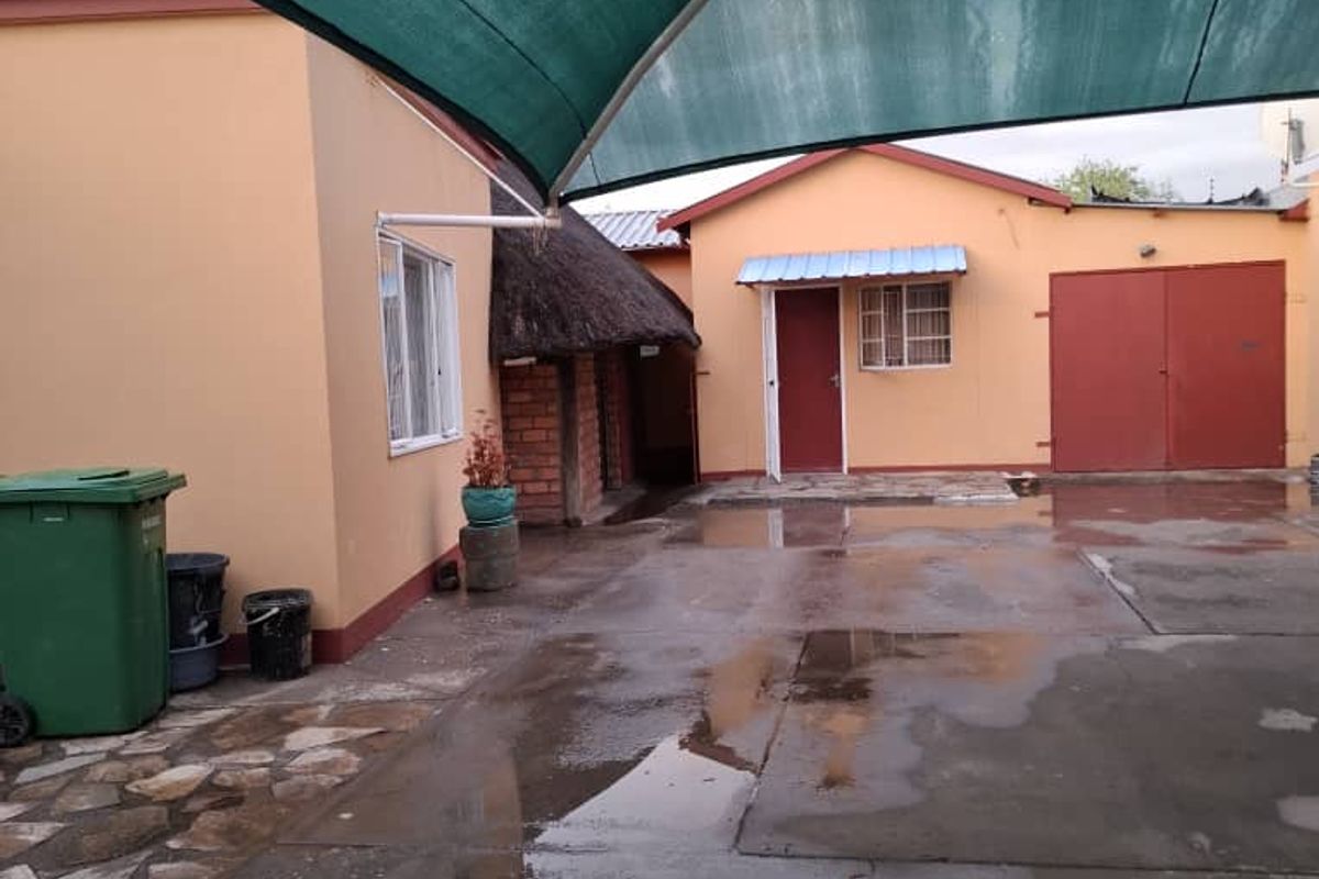 A paved rear courtyard area featuring a large shade sail, concrete driveway, and access to the main dwelling and garage structure.