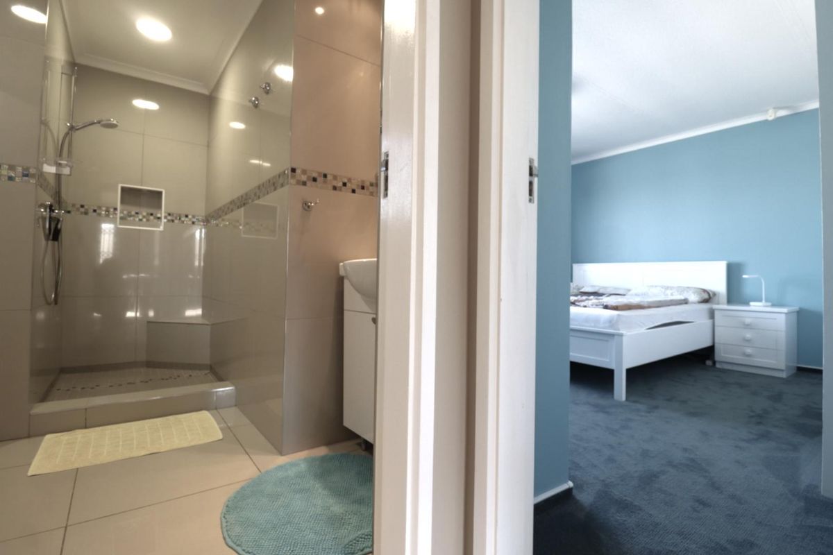 A view from a bedroom into an adjacent modern bathroom featuring a walk-in shower with tiled walls and a vanity unit.