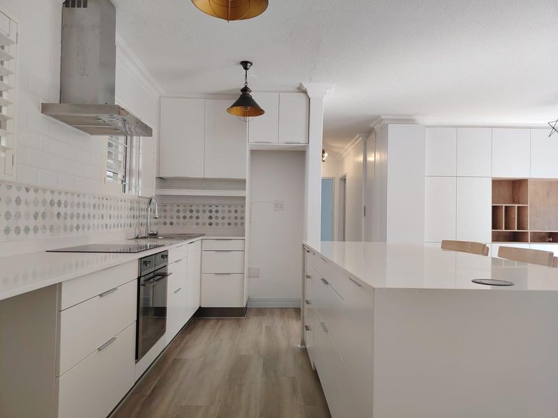 Modern, bright kitchen featuring white cabinetry, stone countertops, integrated appliances, and a central island, finished with contemporary tiling and wood-look flooring.
