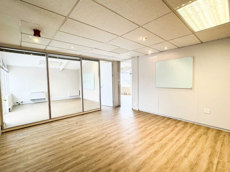 A bright, vacant office space featuring modern laminate flooring, glass partition walls, and a suspended ceiling with integrated lighting.