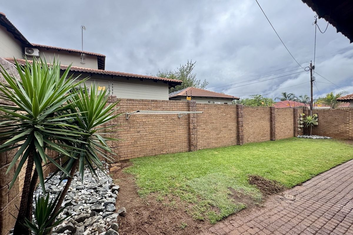 A private rear garden featuring a well-maintained face brick boundary wall with electric fencing, a paved patio area, and a lawn.