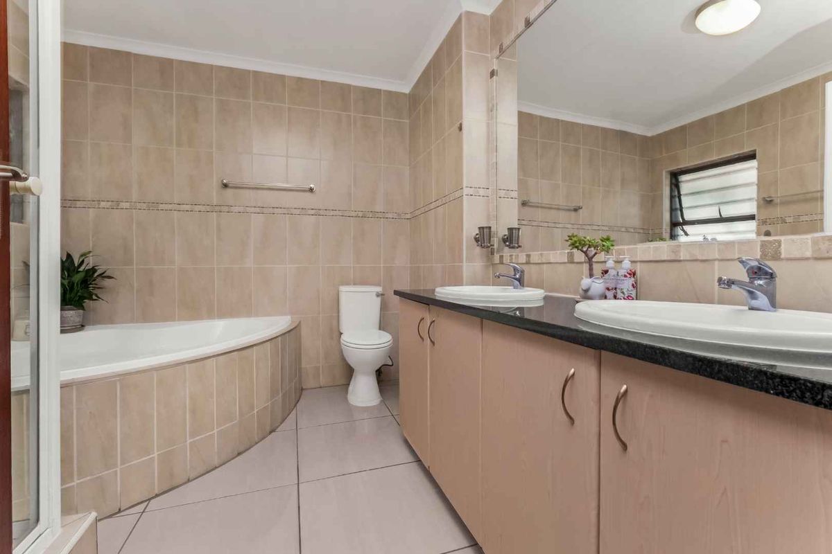 A functional bathroom featuring a corner bathtub, dual vanity with granite countertop, and neutral wall and floor tiling.