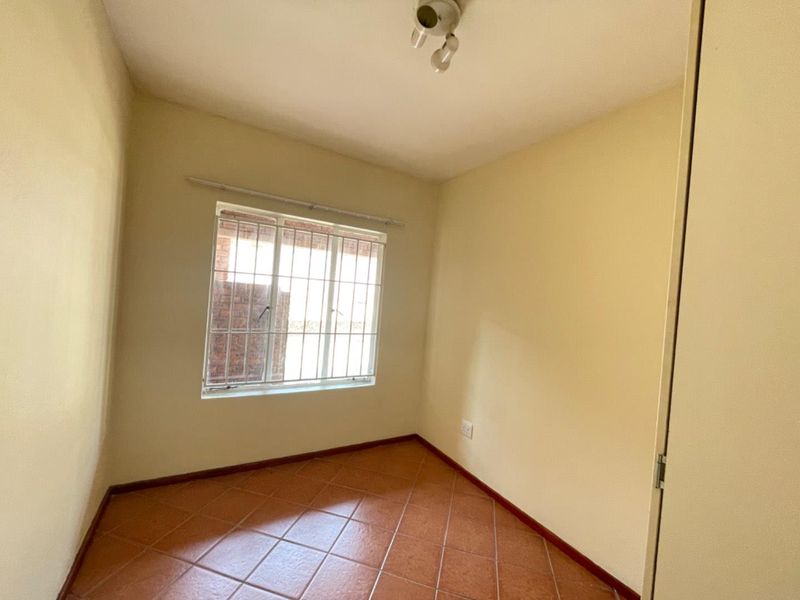 A vacant bedroom featuring tiled flooring, a built-in cupboard, and a window fitted with security bars.