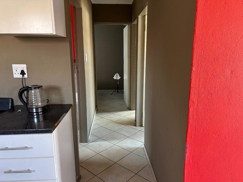 A narrow hallway featuring tiled flooring and access to adjacent rooms, with a small built-in cabinetry section at the entrance.