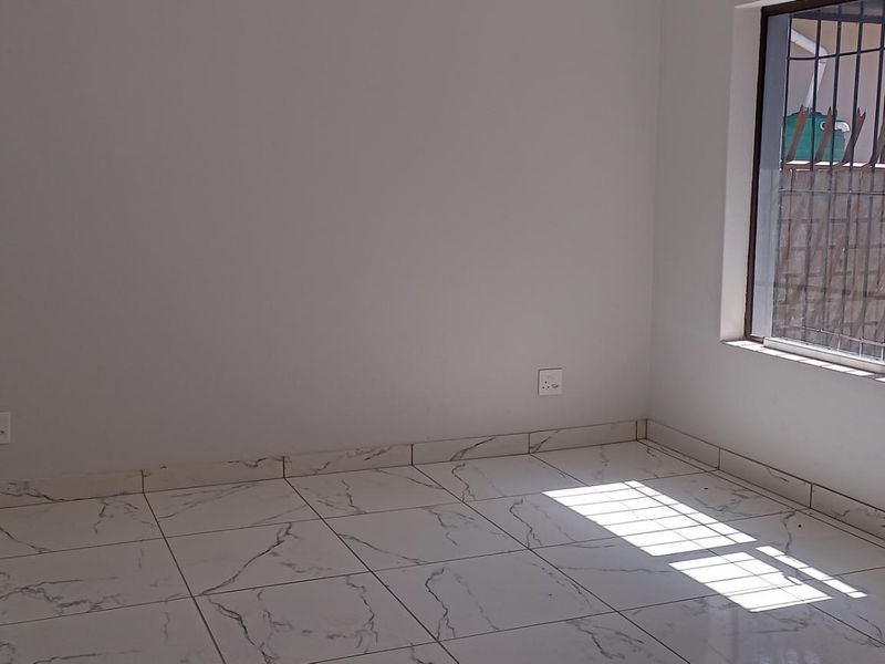A bright, empty bedroom featuring modern marble-look floor tiles, a window with security bars, and a wall-mounted electrical distribution board.
