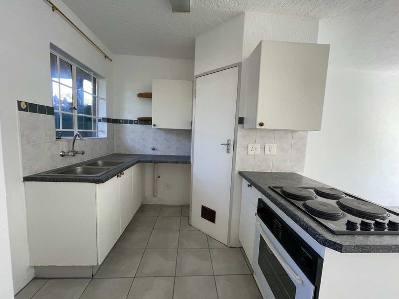 A functional kitchen featuring built-in cabinetry, a double basin sink, and an integrated electric oven and hob with tiled flooring.
