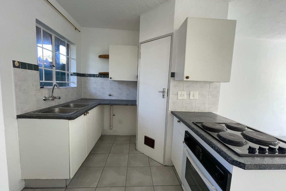 A functional kitchen featuring built-in cabinetry, a double basin sink, and an integrated electric oven and hob with tiled flooring.
