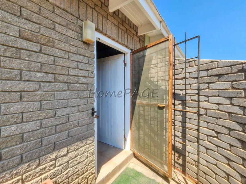 A rear exterior view showing a brick wall, a security gate, and an entrance leading into the property.