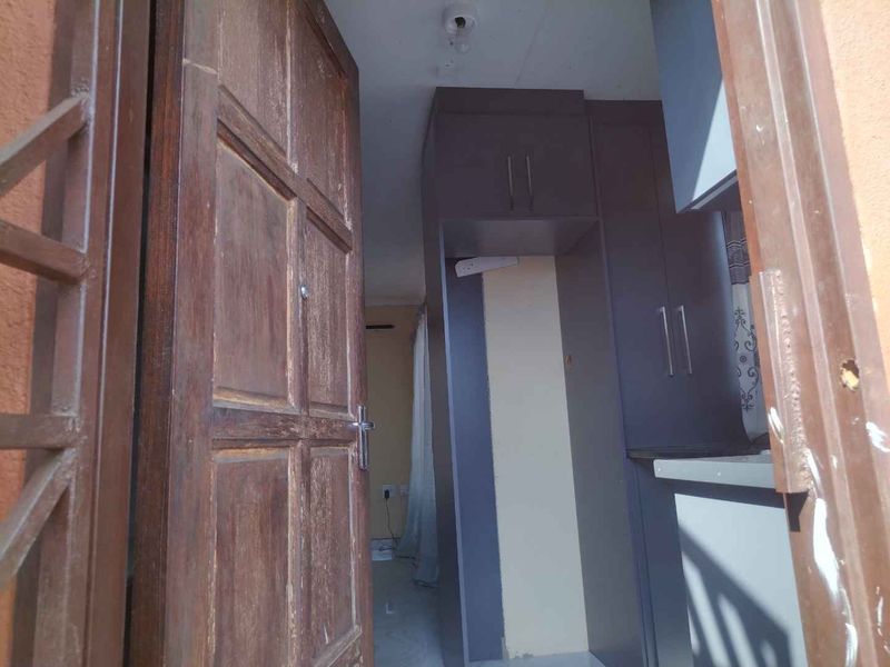 A view through a wooden entrance door into an empty kitchen space featuring dark built-in cabinetry and neutral wall finishes.