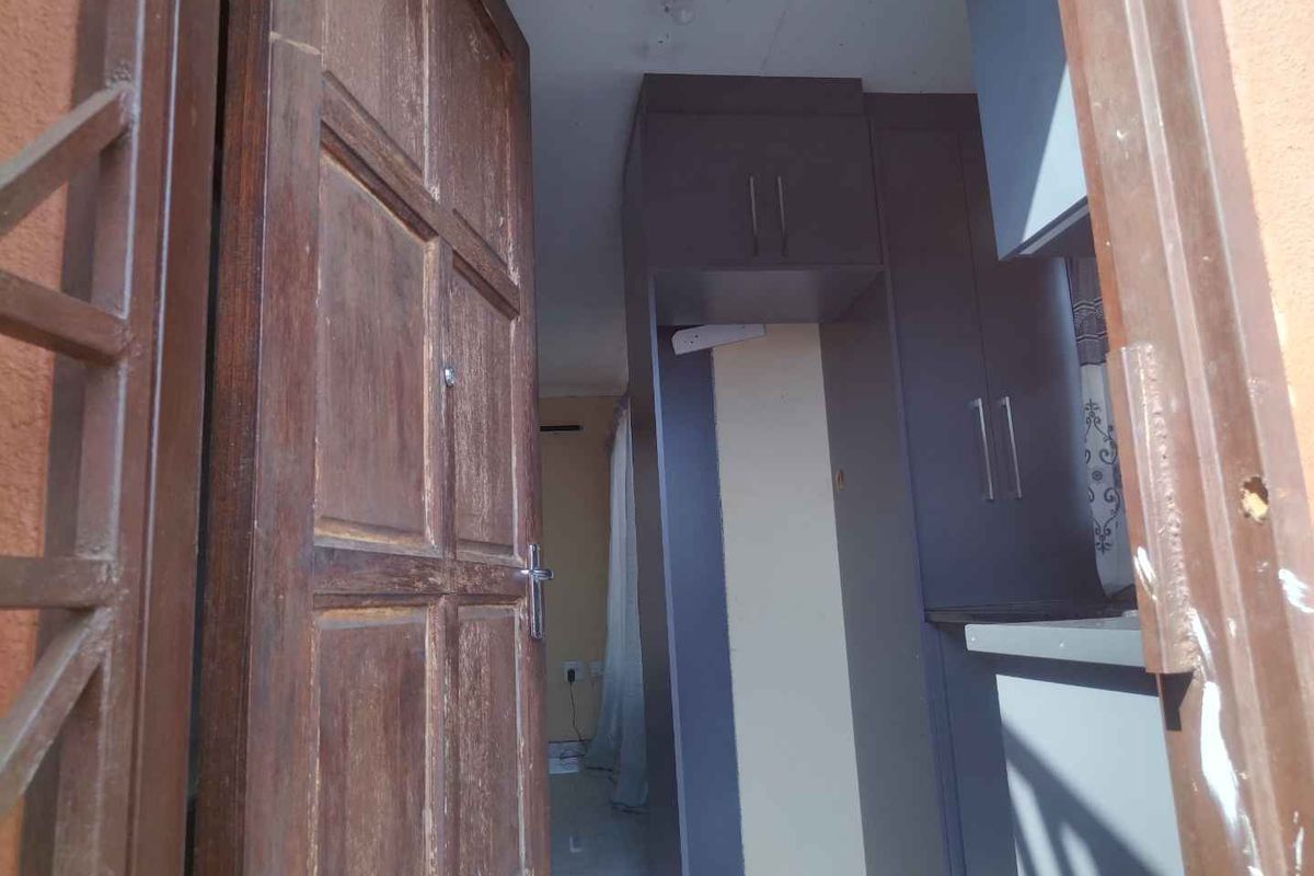 A view through a wooden entrance door into an empty kitchen space featuring dark built-in cabinetry and neutral wall finishes.