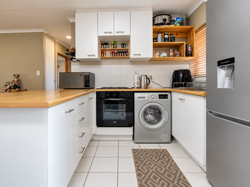 A functional kitchen featuring white cabinetry, laminate countertops, tiled backsplash, built-in oven, gas hob, and an integrated washing machine.