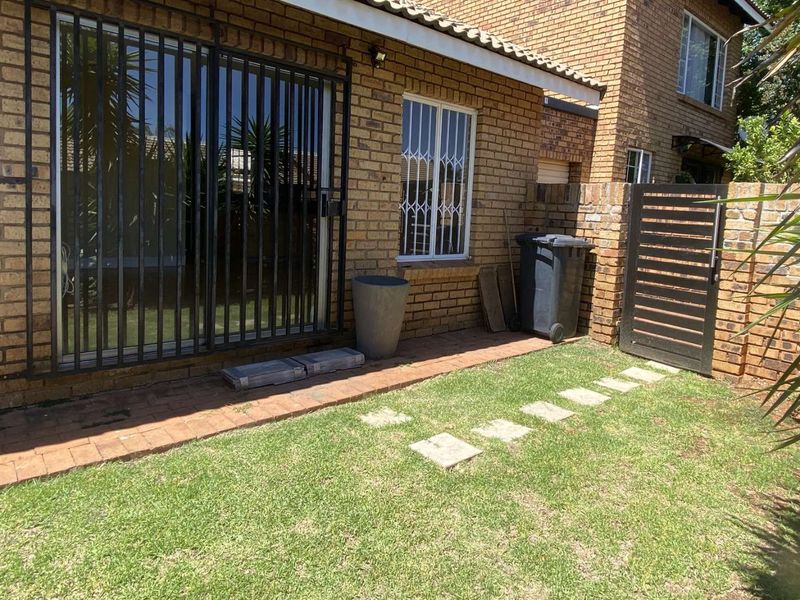 Rear exterior view of the townhouse featuring a brick facade, security gates, sliding door access, and a small private garden area with paved walkway.