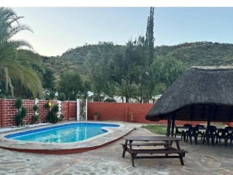 Outdoor pool area featuring a swimming pool, stone paving, and a traditional thatch lapa, set against a scenic mountain backdrop.