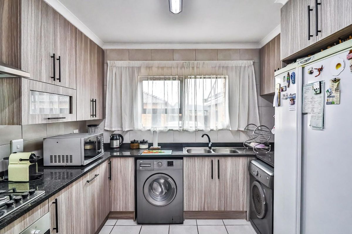 A functional kitchen featuring wood-look laminate cabinetry, granite countertops, a double basin sink, and integrated appliances including a gas hob and oven.
