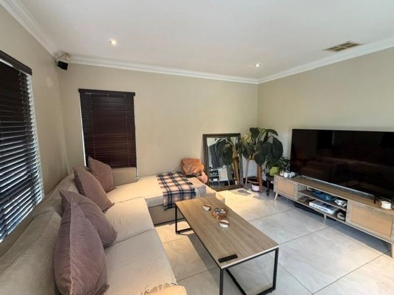 A well-lit living room featuring large format floor tiles, recessed downlighting, and dark venetian blinds, creating a comfortable and functional space.
