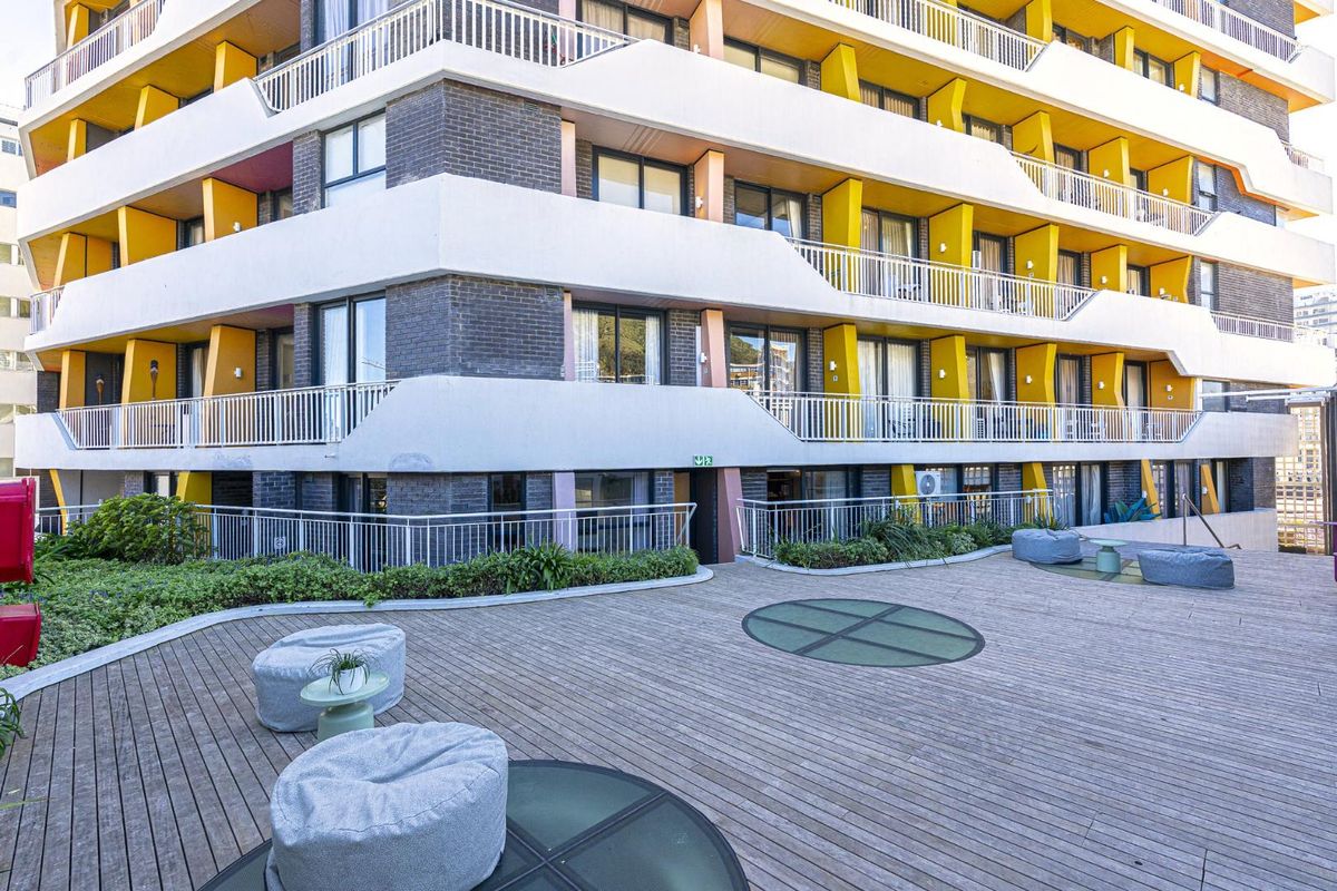 A view of the apartment building exterior featuring a spacious timber deck terrace with integrated glass floor panels and landscaped garden borders.