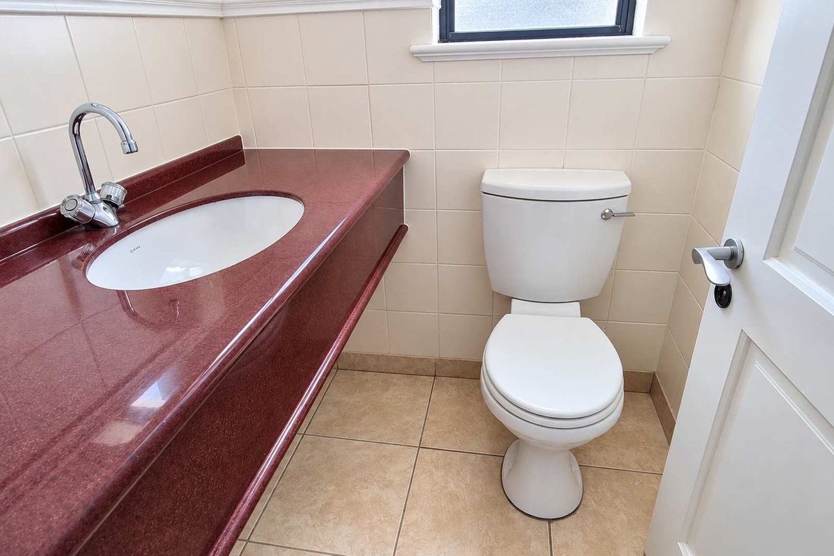 A clean and functional bathroom featuring a red vanity countertop with an integrated sink, a white toilet, and neutral wall and floor tiling.