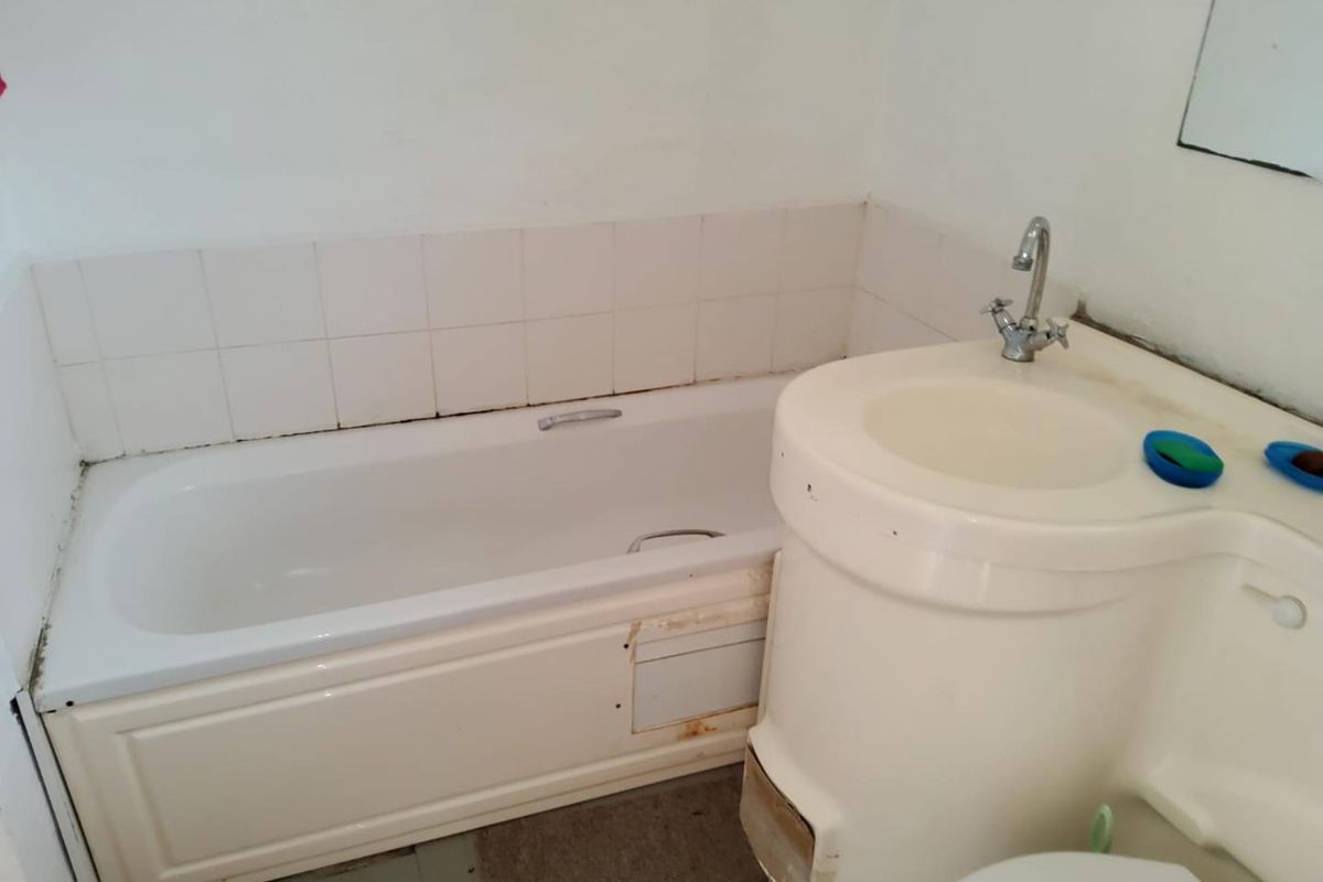 A dated bathroom featuring a standard bathtub with tiled splashback and a compact integrated vanity sink unit.