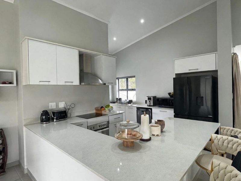 Modern kitchen featuring white cabinetry, quartz countertops, a central island, and integrated stainless steel appliances under a vaulted ceiling.