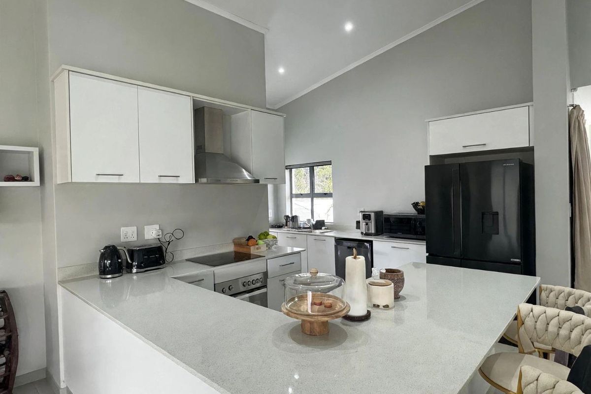 Modern kitchen featuring white cabinetry, quartz countertops, a central island, and integrated stainless steel appliances under a vaulted ceiling.