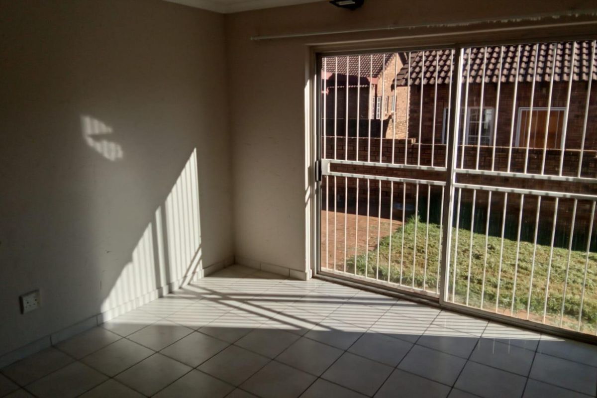 A bright, empty living area featuring tiled flooring and large sliding glass doors with security bars, providing direct access to the rear garden.