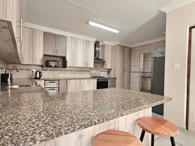 Modern kitchen featuring light wood-grain cabinetry, granite countertops, a breakfast bar, and integrated appliances, with an adjacent scullery area.