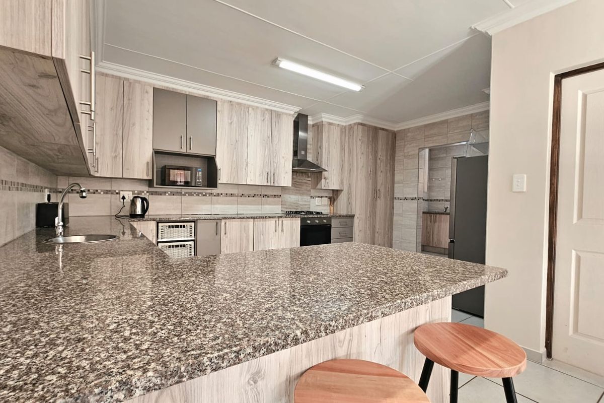 Modern kitchen featuring light wood-grain cabinetry, granite countertops, a breakfast bar, and integrated appliances, with an adjacent scullery area.