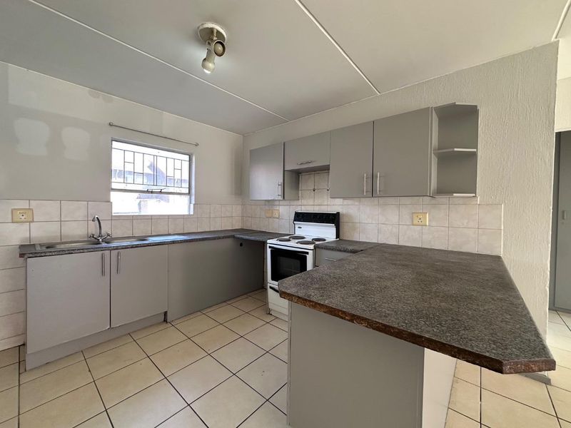 A functional kitchen featuring grey built-in cabinetry, laminate countertops, a tiled backsplash, and a freestanding stove, ready for personal touches.