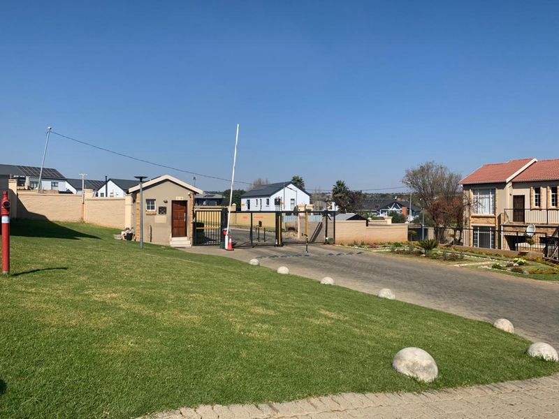 View of the secure gated entrance to the apartment complex, featuring a guard house, boom gate, and paved access road.