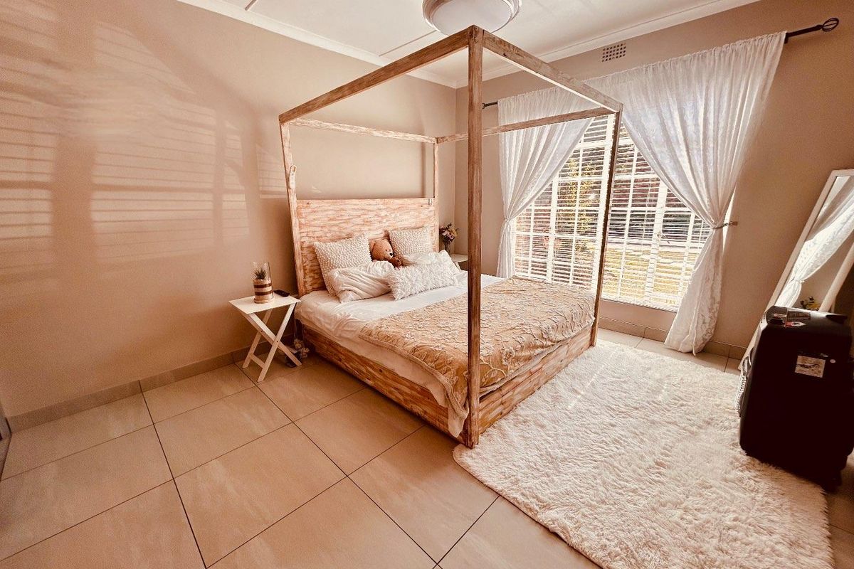 A bright bedroom featuring large windows with security shutters, tiled flooring, and a central ceiling light fixture.