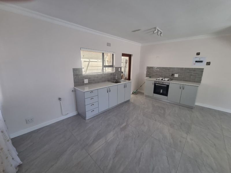 A modern, empty kitchen featuring light grey cabinetry, stone countertops, a built-in oven with gas hob, and neutral tiled flooring throughout.