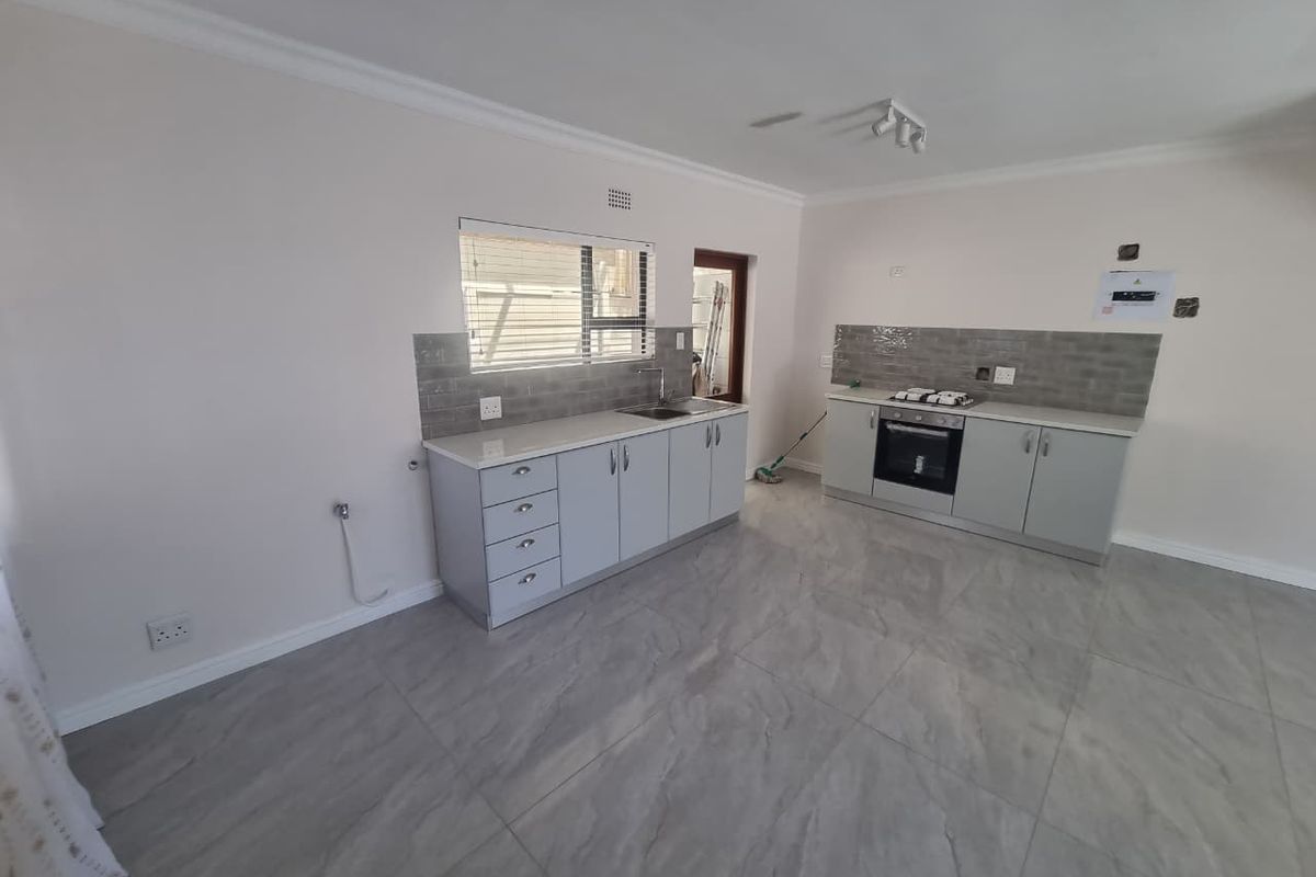 A modern, empty kitchen featuring light grey cabinetry, stone countertops, a built-in oven with gas hob, and neutral tiled flooring throughout.