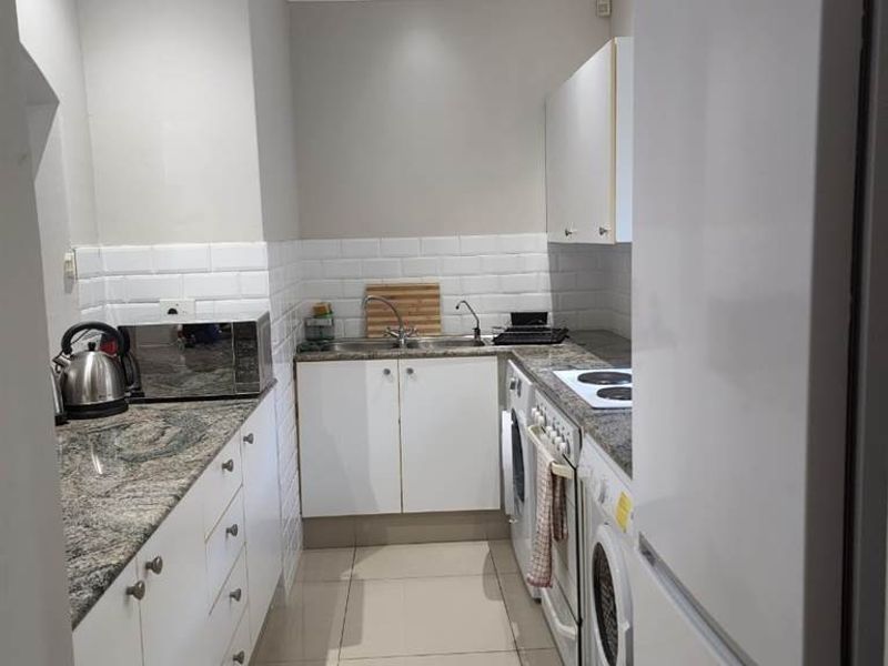 Compact galley-style kitchen featuring granite countertops, white cabinetry, subway tile backsplash, and integrated appliances, offering a functional and clean workspace.