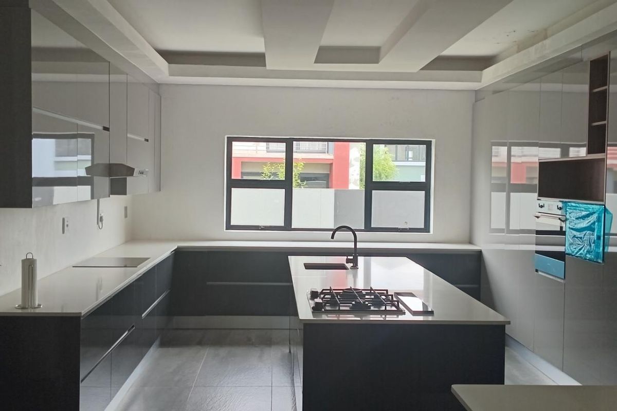 Modern kitchen featuring sleek cabinetry, a central island with a built-in gas hob, stone countertops, and a large window providing natural light.