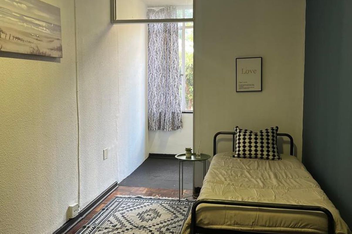 A compact bedroom featuring dark parquet flooring, a feature wall, and an adjoining small sunroom or enclosed balcony area.