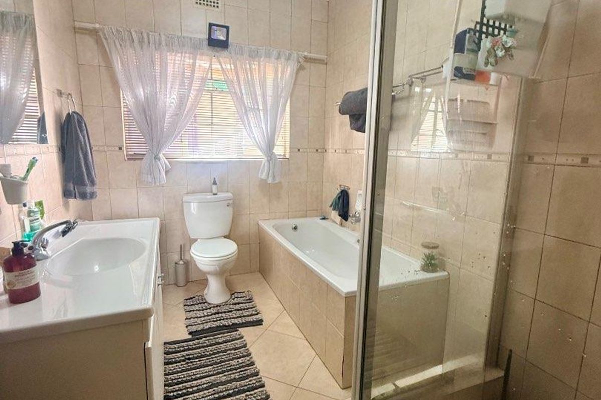 A functional bathroom featuring a built-in bathtub, separate glass-enclosed shower, vanity basin, and toilet with neutral wall and floor tiling.