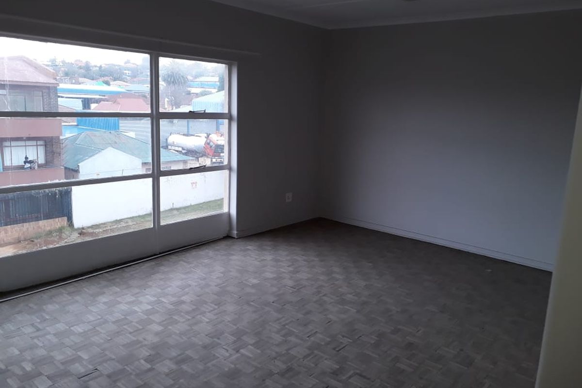 An empty living room featuring classic parquet flooring and a large window providing natural light and an urban view.