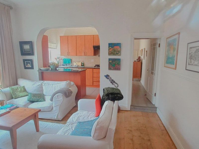 Open-plan living area featuring wooden floors and an arched transition to a functional kitchen with built-in cabinetry and tiled backsplash.