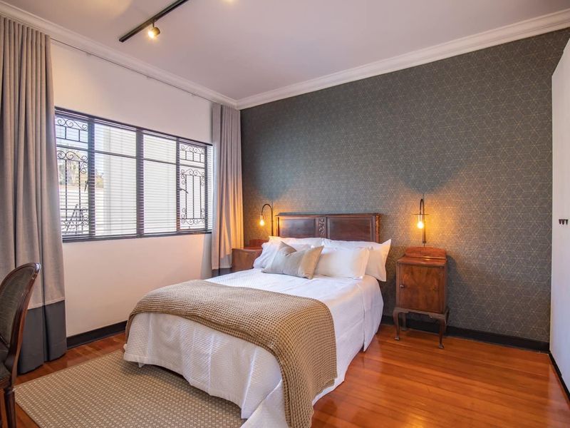 A well-maintained bedroom featuring polished hardwood flooring, crown molding, track lighting, and a feature wall with patterned wallpaper.