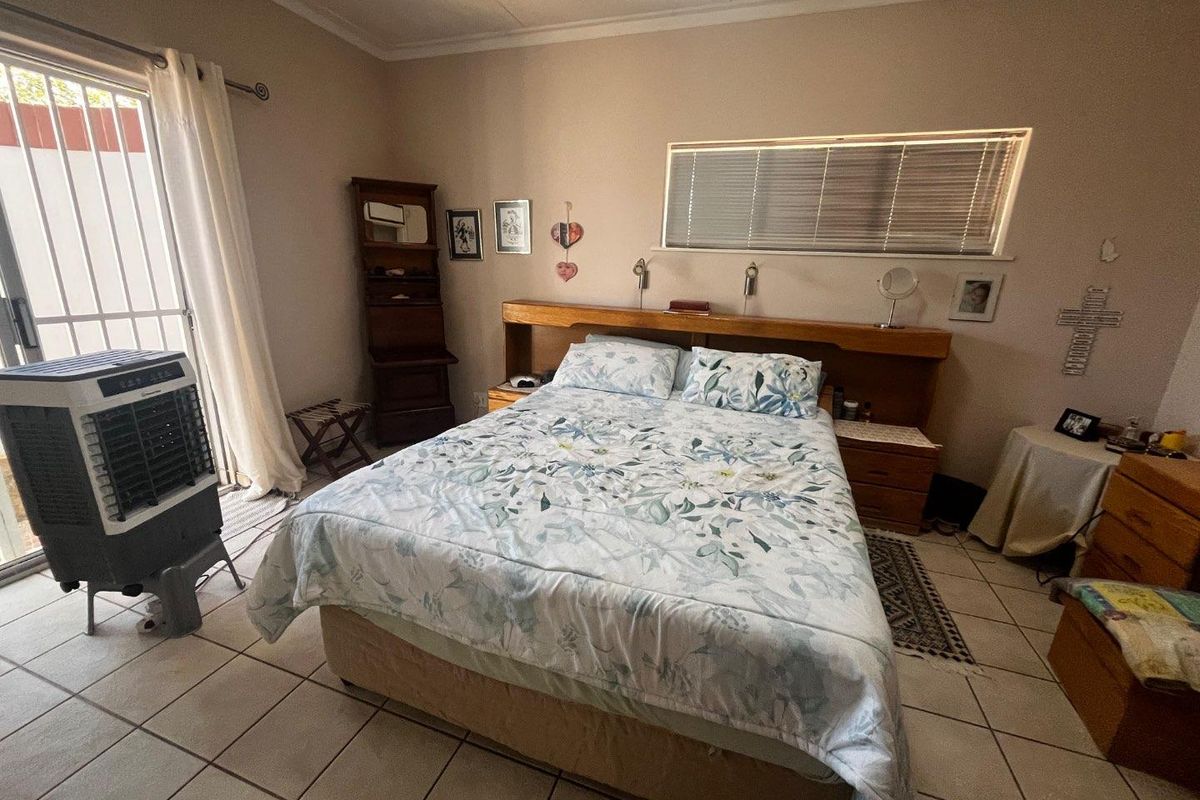 A bedroom featuring tiled flooring, a built-in wooden headboard with integrated lighting, and a sliding glass door providing access to the exterior.