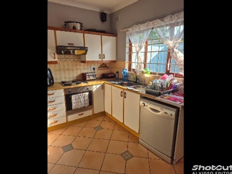 A functional kitchen featuring built-in cabinetry, a hob, oven, extractor fan, and tiled flooring. The space offers a practical layout with ample storage.